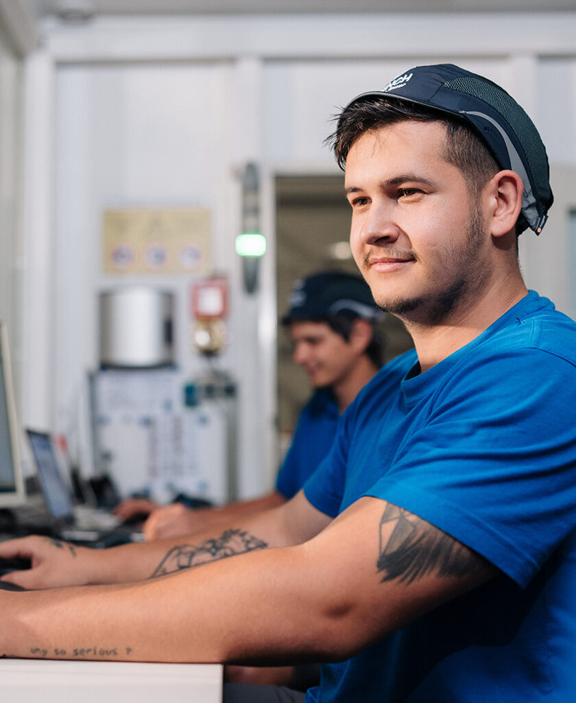 young worker sits on a desk and looks at a hidden screen, colleague in the background