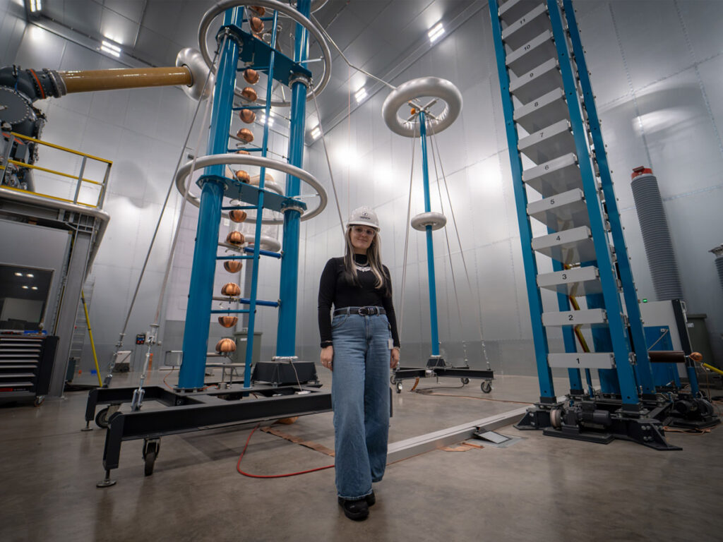 Victoria Bold standing among high-voltage testing equipment at Trench Group's Bamberg facility.