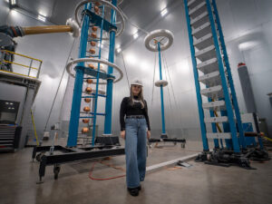 Victoria Bold standing among high-voltage testing equipment at Trench Group's Bamberg facility.