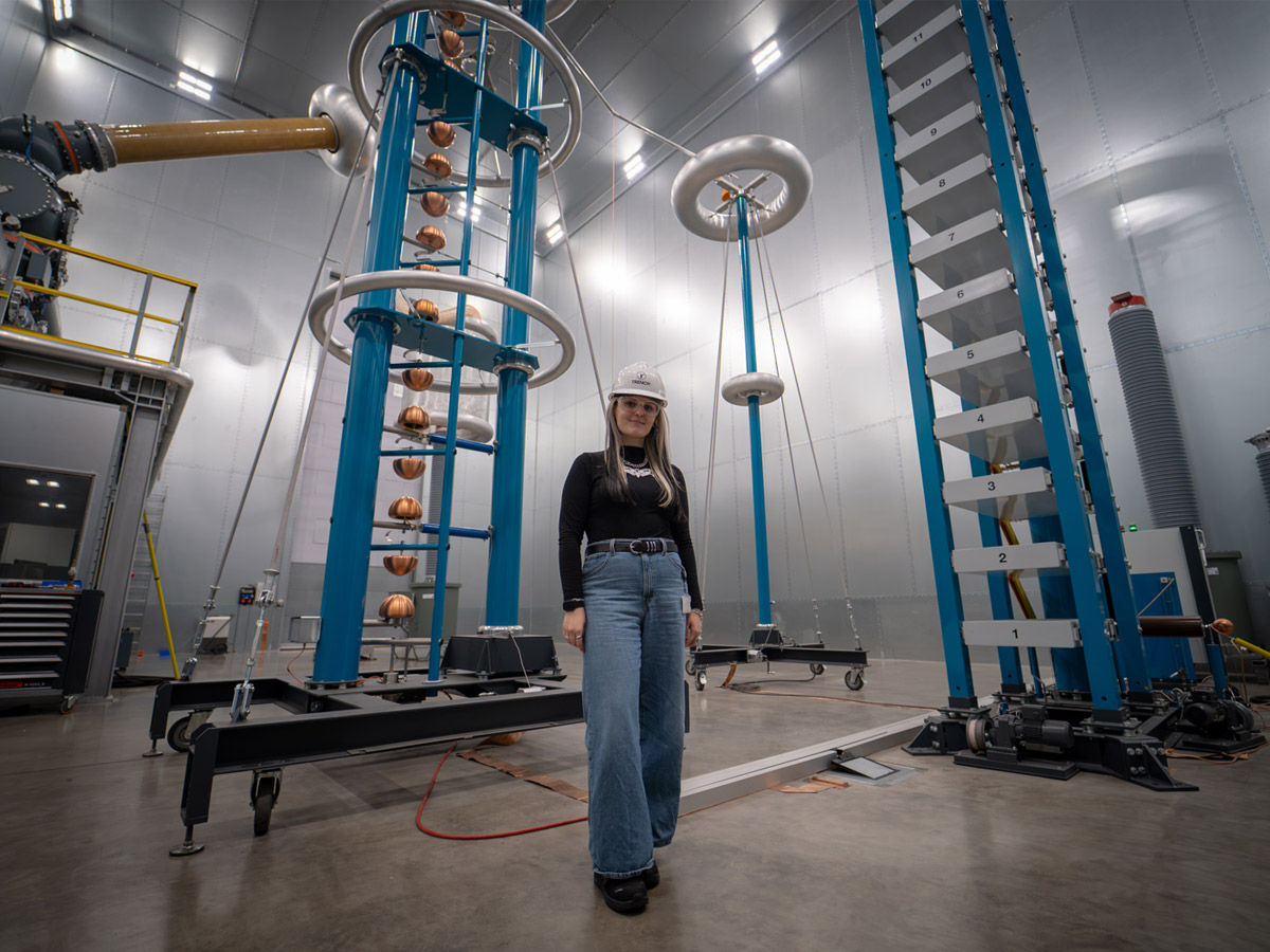 Victoria Bold standing among high-voltage testing equipment at Trench Group's Bamberg facility.